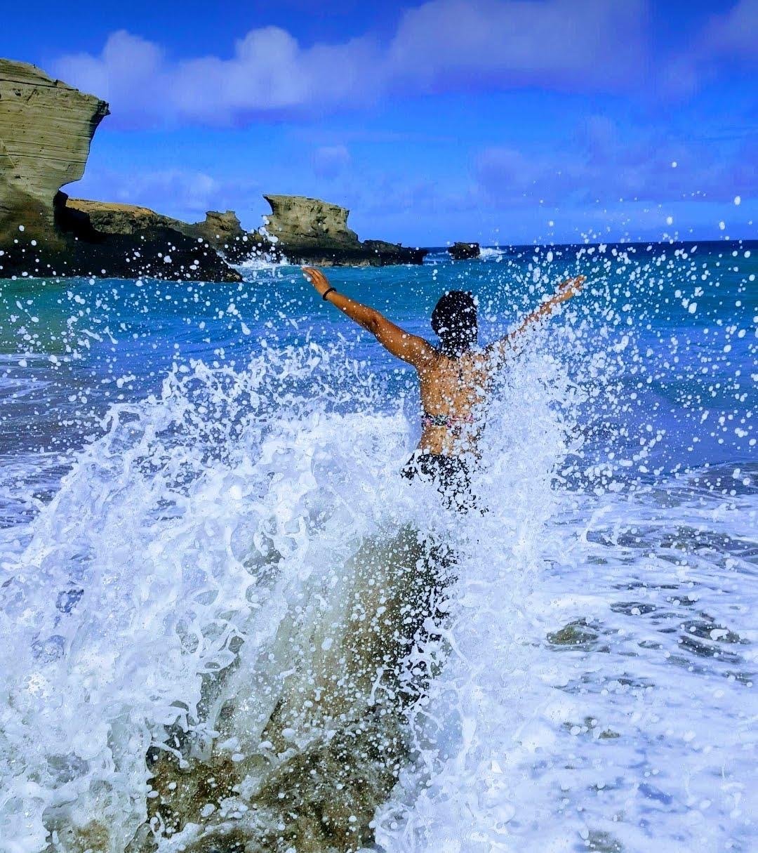 Traveler joyfully embracing ocean waves beneath a blue sky